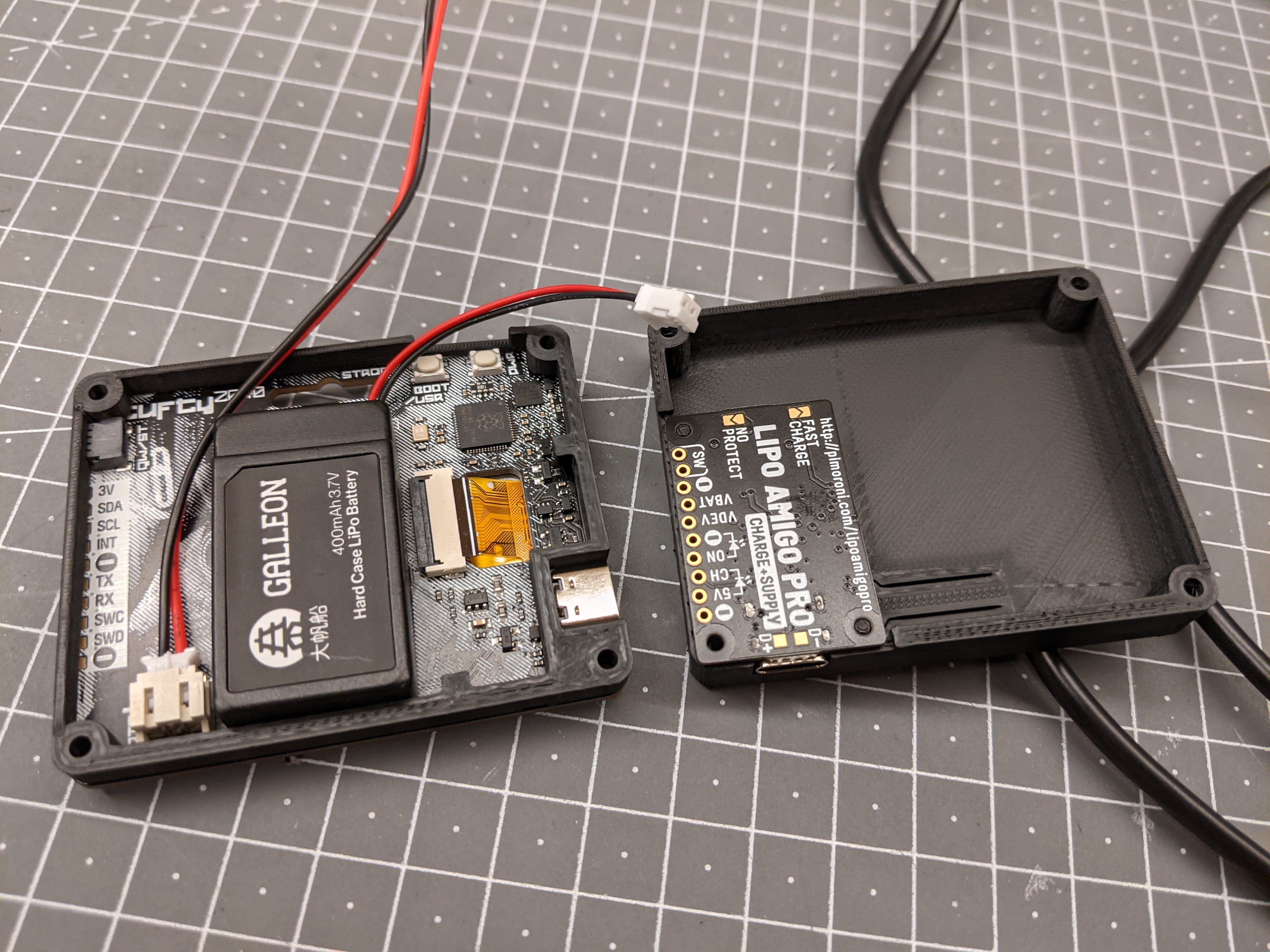 The two halves of the case opened, with the back of the Tufty and the mid piece and battery on one side, and the Amigo sat words-up in the case back on the other.